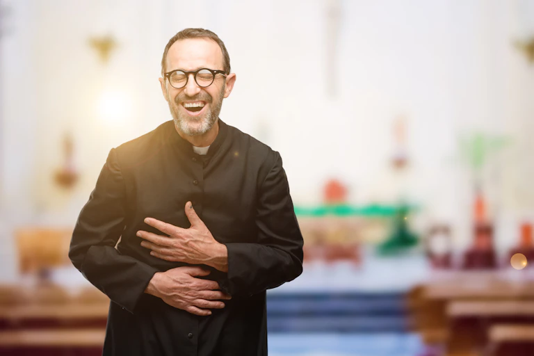 A man in a Catholic priest robe laughs in a church