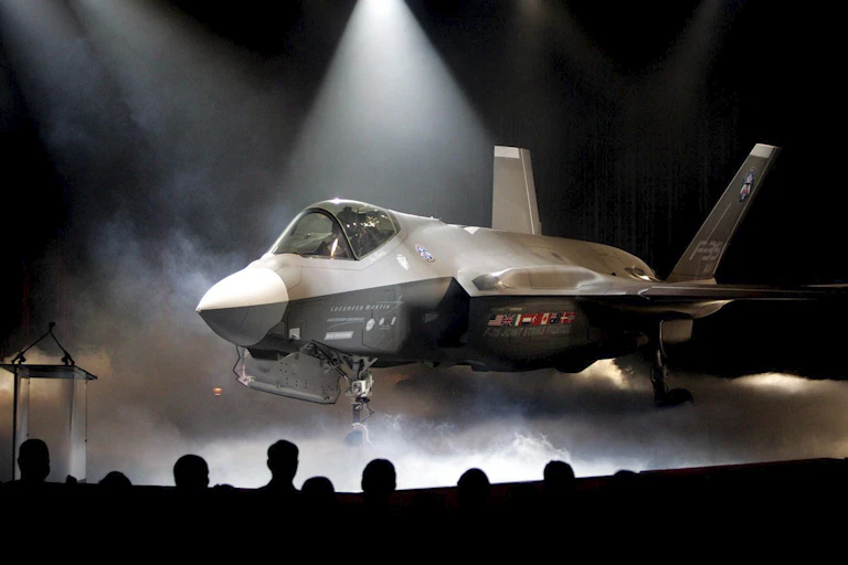 A fighter jet sit on a stage under spotlights and enshrouded in dry ice.