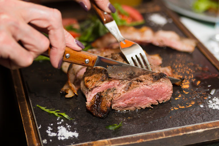 A close-up of a woman cutting meat with a fork and knife.
