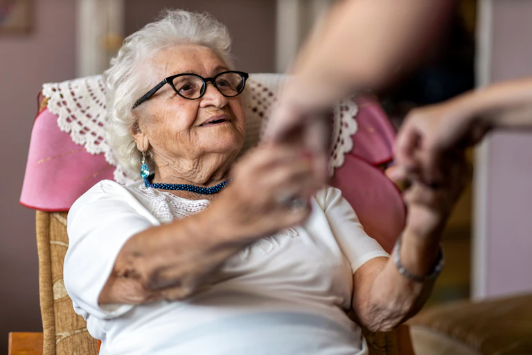 A woman with gray hair and glasses reaching out to take the hands of a person out of frame