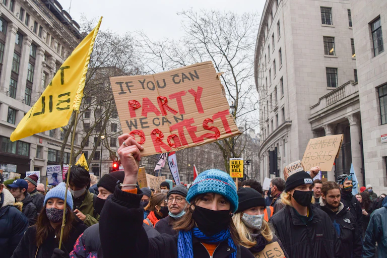 A woman at a protest holding a sign reading 'if you can party, we can protest'.