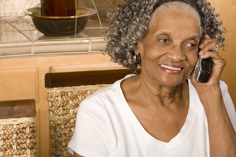 A woman with gray hair smiling while holding a telephone to her ear.