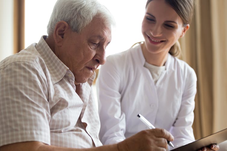 A man with gray hair holding a pen while a younger woman smiles beside him