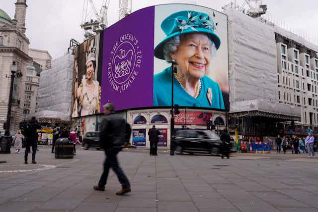 A billboard shows two photos of Queen Elizabeth, one young and one old.