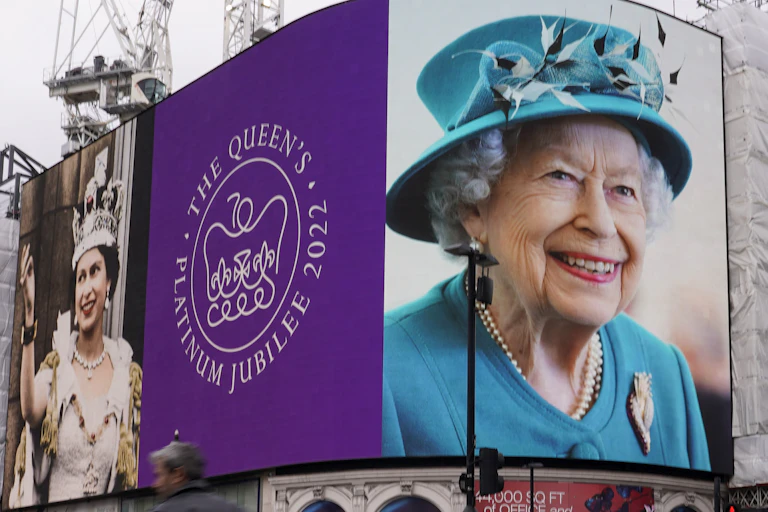 A billboard shows two photos of Queen Elizabeth, one young and one old.
