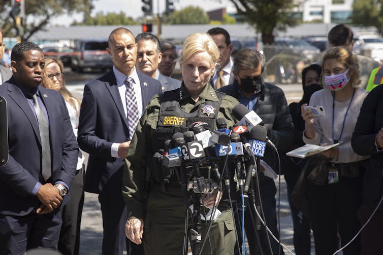 A woman in a police uniform stands at a bank of microphones