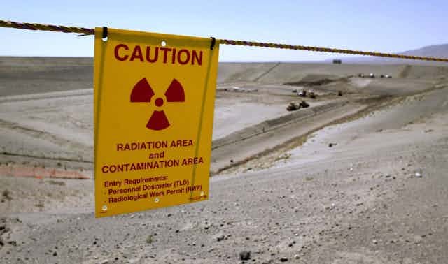 A yellow sign says Caution, radiation area and contamination area, in front of a large swath of dirt and grey land.