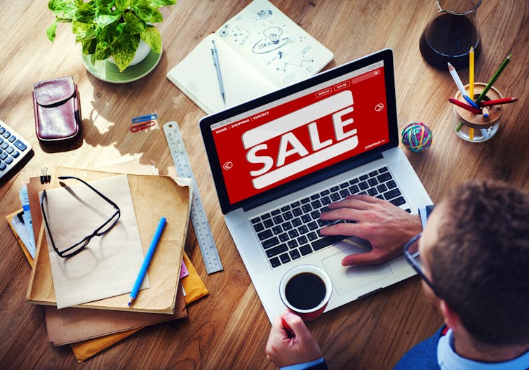 A male shopping on his laptop which displays a sale sign