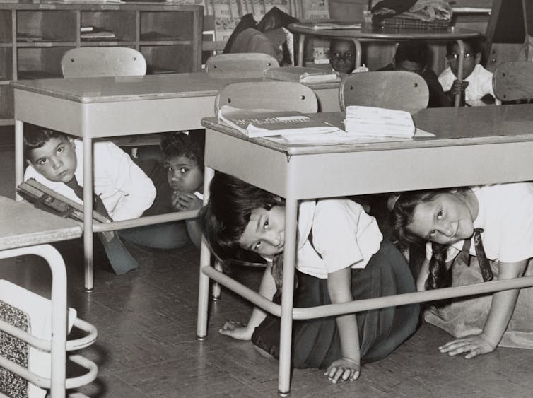 Young students are seen hiding under their desks and looking out in this black and white photo