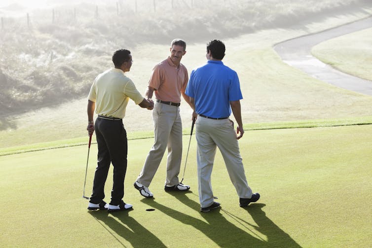 Three men on a golf course and two shaking hands.