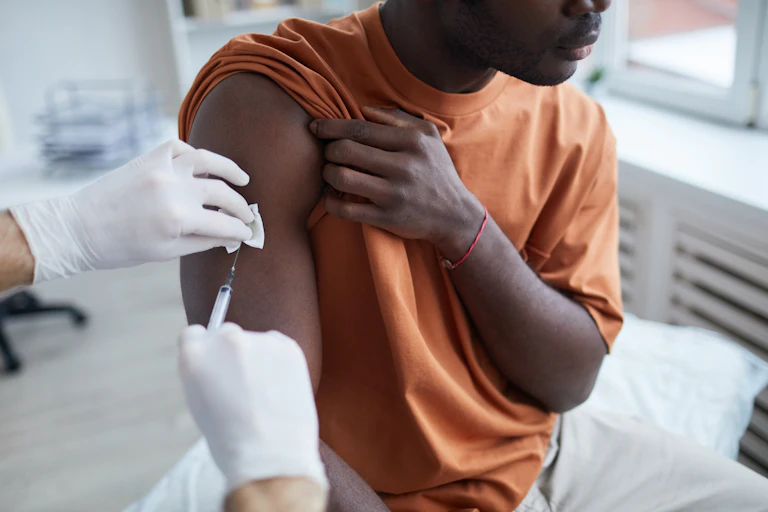 African Australian man in an orange tshirt raises his sleeve to get vaccinated.