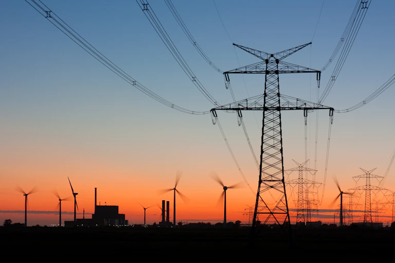Líneas de cables eléctricos y molinos al fondo al atardecer