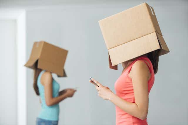 Jóvenes con móviles en la mano y cajas de cartón en la cabeza