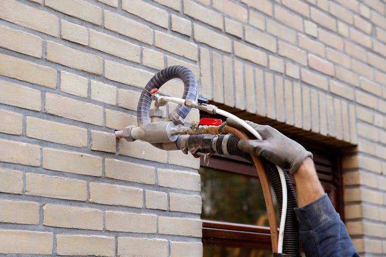 A gloved hand holds a tool injecting cavity wall insulation into brickwork.