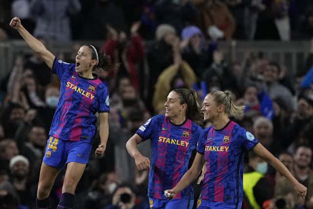 Three women football players in front of crowd