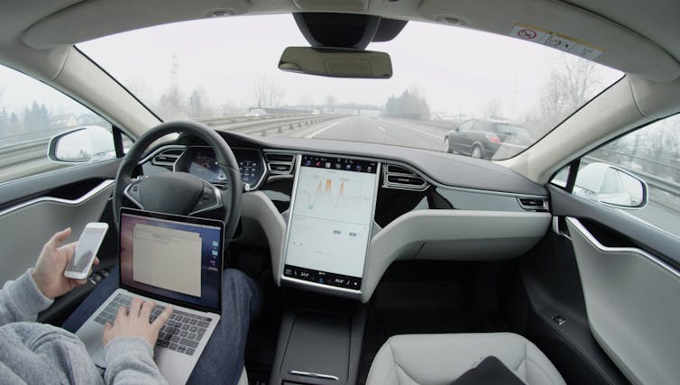 view from the cockpit of a tesla with another car ahead and the driver working on their devices