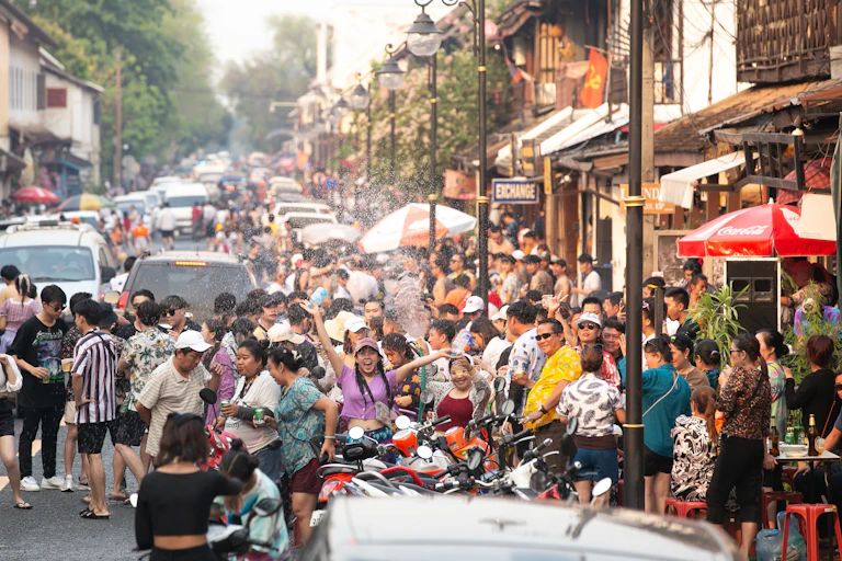 A crowded street with people dressed in colorful clothes sprinkling water on each other during the Songkran Festival in Luang Prabang, Laos.