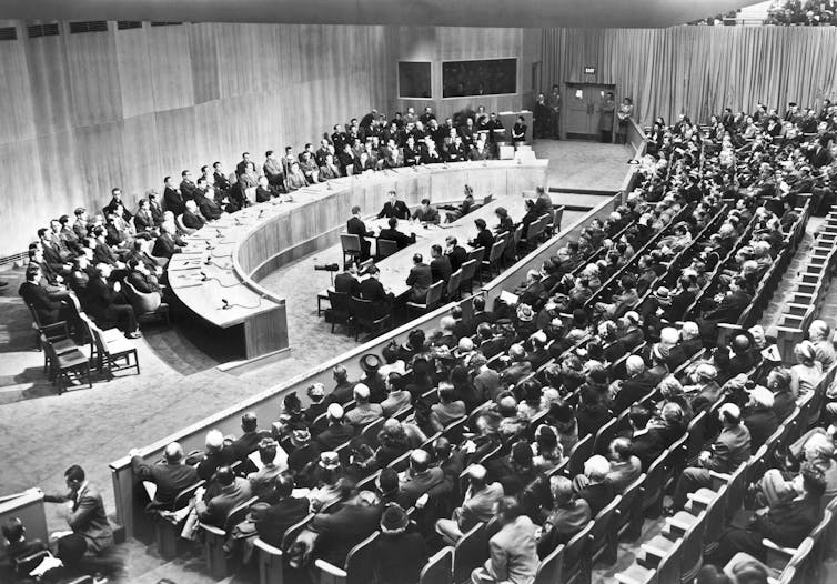 A large meeting room with a semicircle table in front and rows of seats looking on