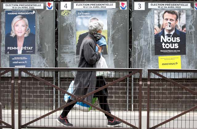 A woman with shopping bags walks past posters of the main candidates in the French presidential election.