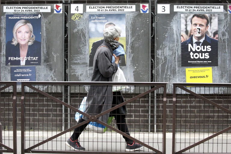 A woman with shopping bags walks past posters of the main candidates in the French presidential election.