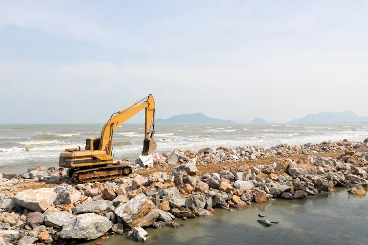 Construction equipment sits atop an ocean barrier made of large rocks