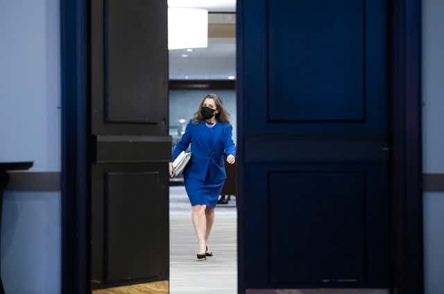 A woman dressed in blue walks towards a partially opened door