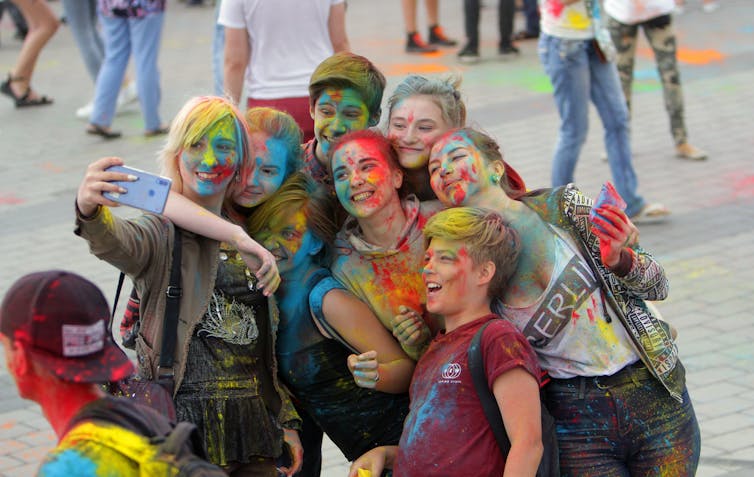 Several teenagers, smiling and wearing face paint, take a group photo.