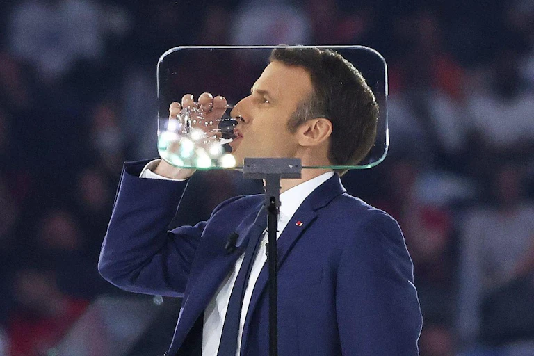 Macron drinking from a glass of water behind an autocue
