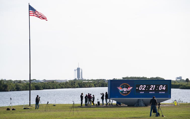 A countdown timer in front of a small lake, a rocket visible in the background