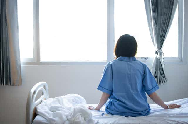 Una mujer de espaldas sentada en la cama de un hospital.