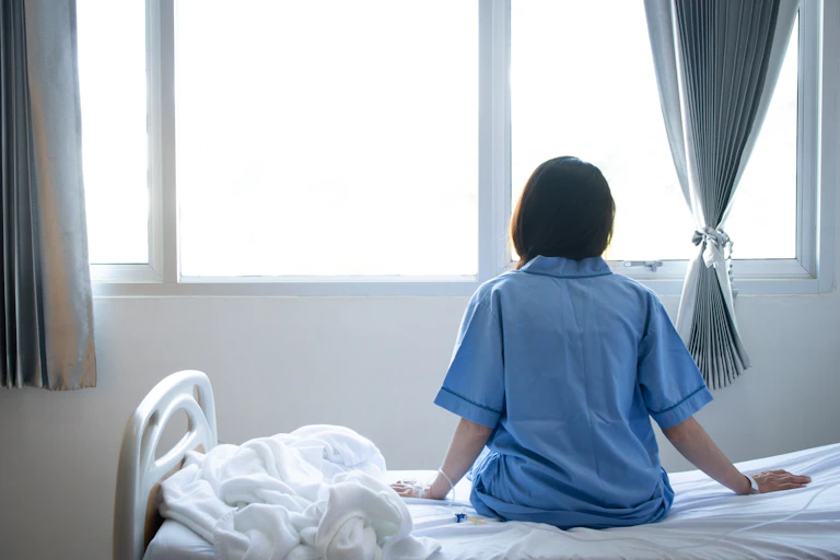 Una mujer de espaldas sentada en la cama de un hospital.