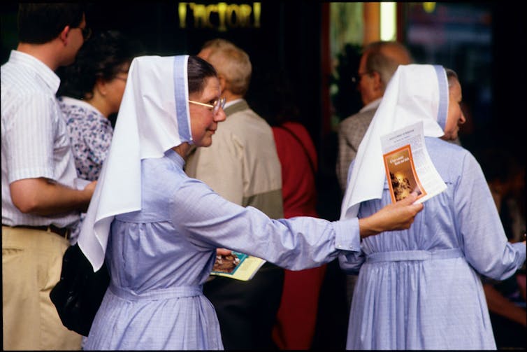 Two Catholic nuns wearing head coverings pass out brochures.