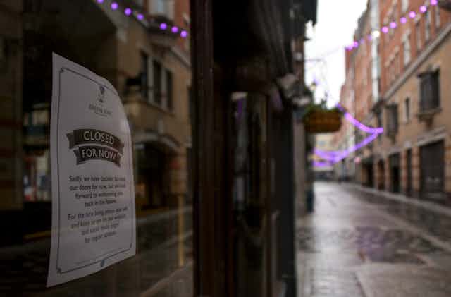 a sign on a pub window reads 'closed for now' along a deserted cobblestone street