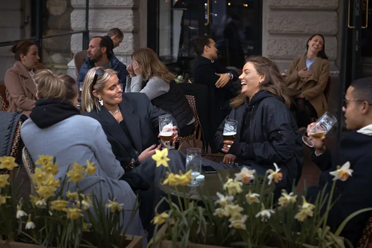 women chat and laugh on a restaurant patio with potted daffodils in the foreground