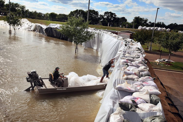 A person in a boat checks the river side of sandbag levee protecting a community during a flood.