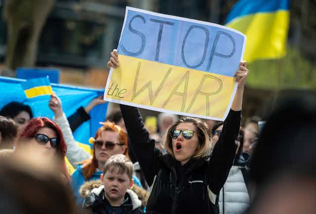 Person holding sign of Ukraine flag saying 'stop the war'