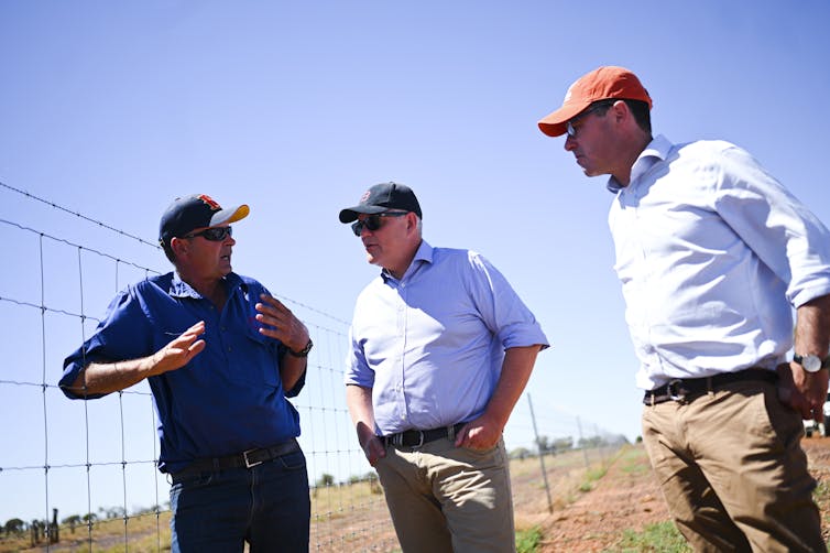 three men stand next to wire fence