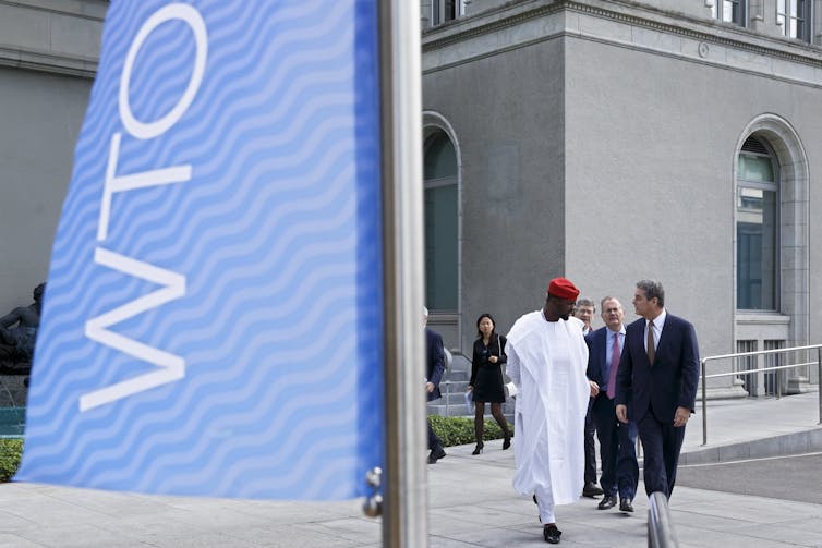 Two people walk past WTO sign