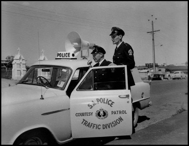 policemen in uniform, standing by a police car