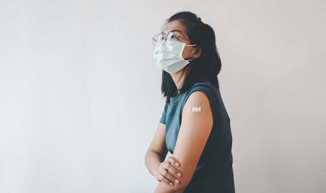 A young woman wearing a mask with a bandaid on her upper arm.
