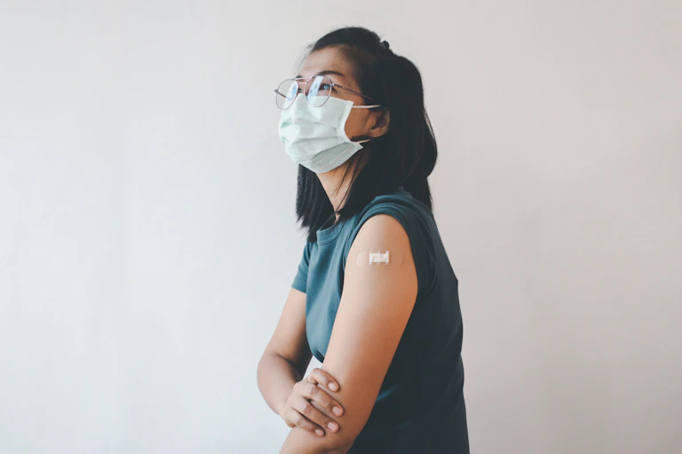A young woman wearing a mask with a bandaid on her upper arm.