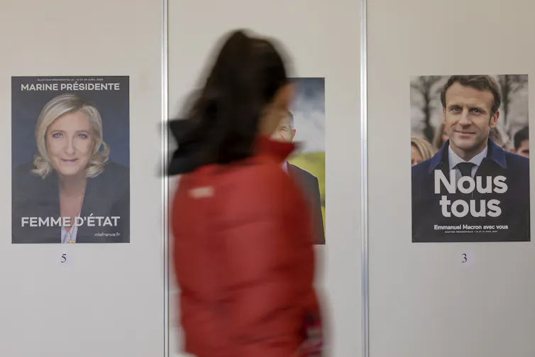 A woman stands in between two election posters – one depicting Marine Le Pen and the other, Emmanuel Macron.