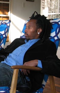 A man in a blue shirt reclines in a blue and white chair, gazing ahead.