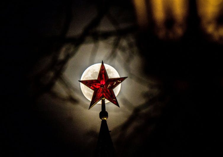 Red star on spire silhouetted by tree cover.