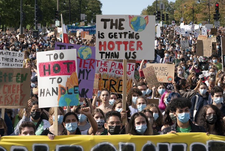 A crowd of people seen at a demonstration, with some youth holding a sign saying 'too hot to handle.'