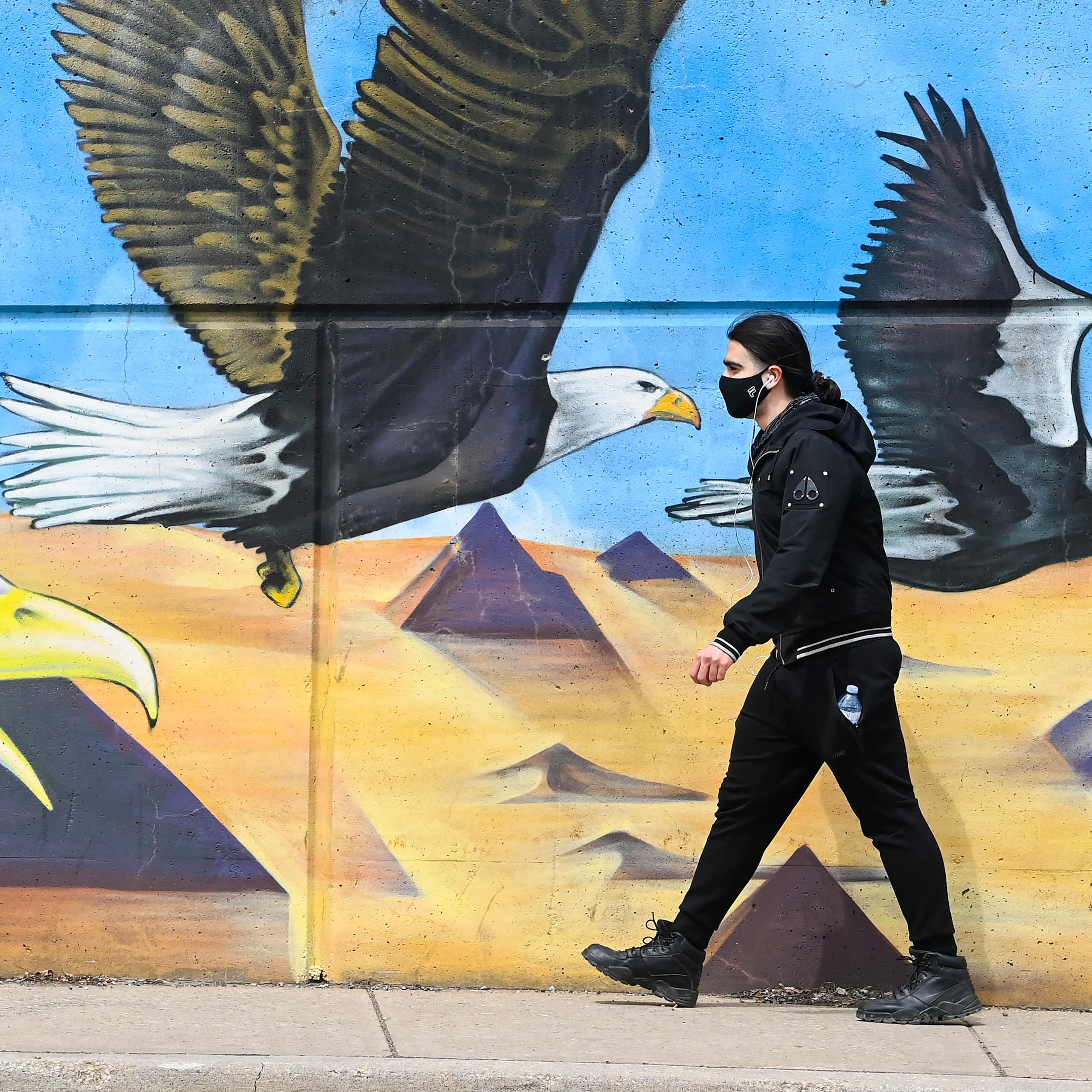 A person wearing a face mask strides past a mural showing giant eagles flying towards them