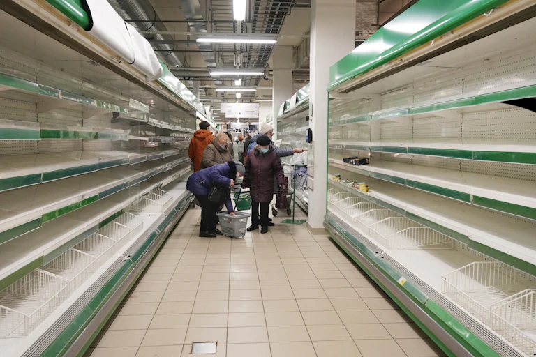 People stand at the end of a grocery store aisle with empty shelves