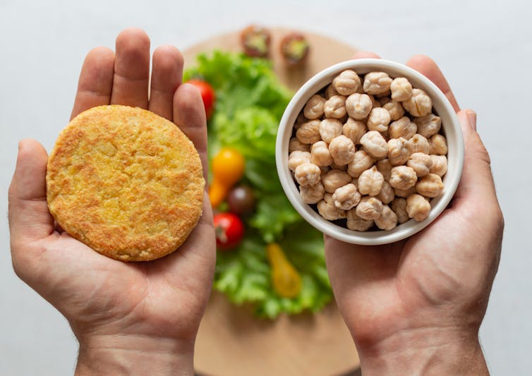 A bird's eye view of a plant-based patty in one hand and a cup of legumes in the other hand.