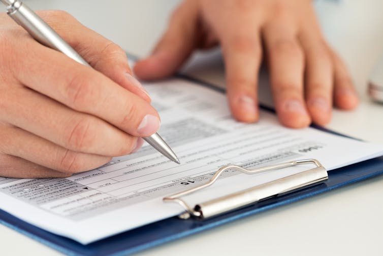 Close up of a man filling out a paper form.