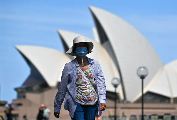 Woman in a facemask walks past the Sydney Opera House